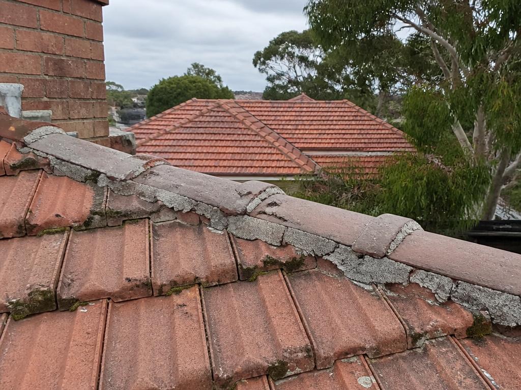 Weathered terracotta tile roof with cracked and crumbling cement pointing along the ridge capping